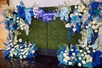 A flower wall featuring the event's 'Experience More' tagline welcomed guests to an evening reception.