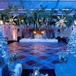 Sometimes, leaning into the season through cozy, winter-inspired decor can add a natural warmth to your event design. For a corporate holiday party held in December 2023, Sterling Engagements created a stylish wintry retreat in a lodge-like setting. The space featured snow-dusted trees, serene blue lighting inspired by the winter sky, and a color palette complemented by shimmering metallics that were designed to catch the light. The centerpiece of the festive gathering was the plaid dance floor and eye-catching ceiling installation, which mixed different mediums including winter greens, pine cones, starbursts, and more. Florals furthered the whimsical, wintry theme.