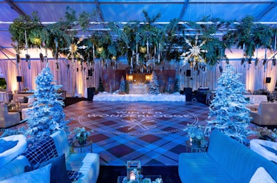 Sometimes, leaning into the season through cozy, winter-inspired decor can add a natural warmth to your event design. For a corporate holiday party held in December 2023, Sterling Engagements created a stylish wintry retreat in a lodge-like setting. The space featured snow-dusted trees, serene blue lighting inspired by the winter sky, and a color palette complemented by shimmering metallics that were designed to catch the light. The centerpiece of the festive gathering was the plaid dance floor and eye-catching ceiling installation, which mixed different mediums including winter greens, pine cones, starbursts, and more. Florals furthered the whimsical, wintry theme.
