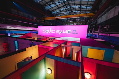 In early December, more than 4,000 fans experienced the Squid Game Maze in The Netherlands. The interactive maze was made up of tasks designed to test guests' capabilities to become a pink guard. The 20 corridors and rooms included a dormitory, playground, and cave inspired by the series. Recruits were challenged to reach the end of the maze as quickly as possible while also getting a taste of what it's like to be in the world of Squid Game.