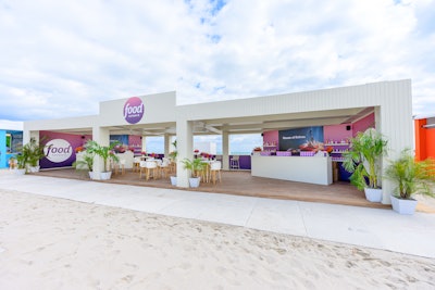 Food Network’s build on the beach was once again helmed by CH CRE8TIVE and featured oversize printouts of select shows and talent. Attendees flocked to the activation to score insulated pink and purple ombre-style wine tumblers (which matched the design scheme) filled with custom cocktails while munching on snack mix.